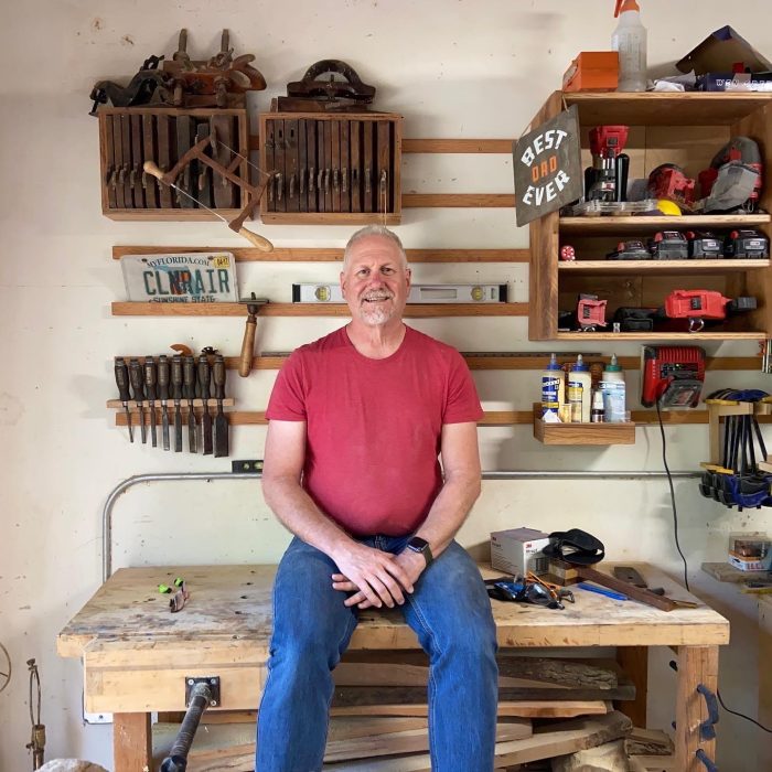 Jonathan Lyons sitting on his workbench, surrounded by tools.