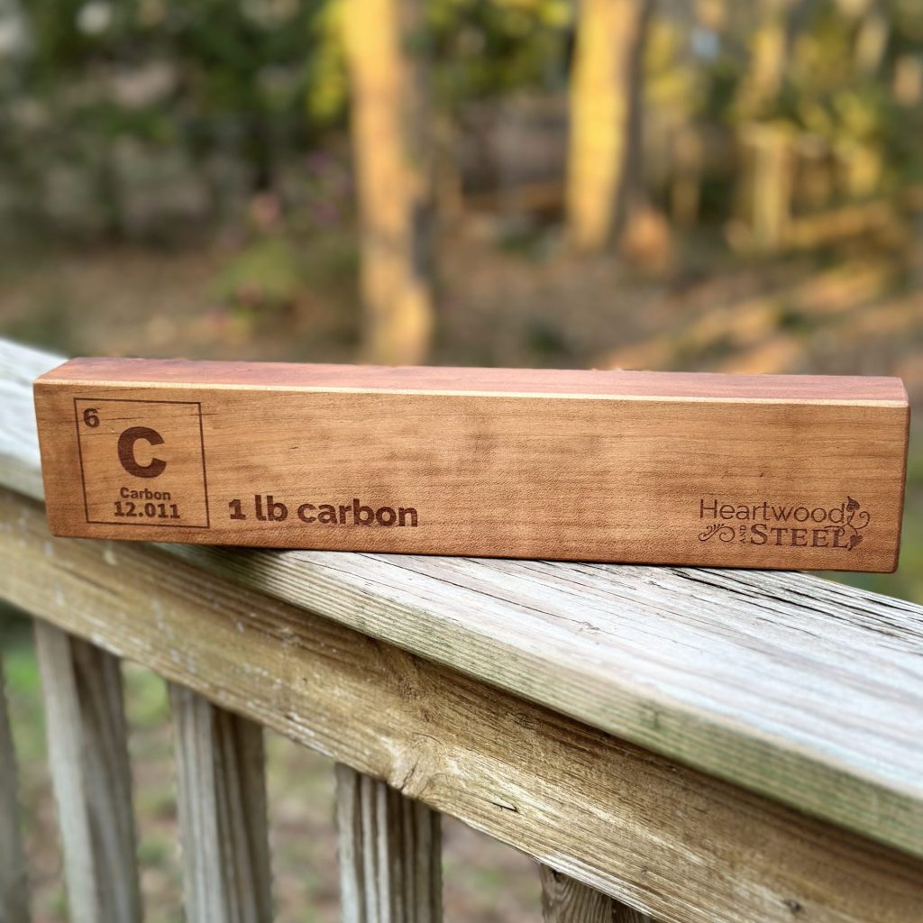 A block of wood which is engraved with the chemical symbol for carbon, "1 lb Carbon" and the Heartwood and Steel logo.